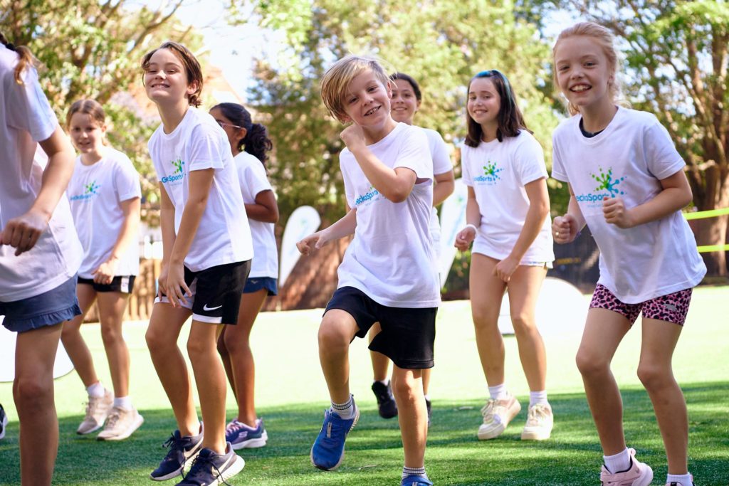 GeckoFIT kids fitness session Children in GeckoSports t-shirts doing an outdoor group fitness game on a grassy field.